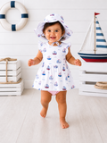 Smiling toddler in a sailboat-patterned dress and hat, playing in a bright, nautical-themed room.