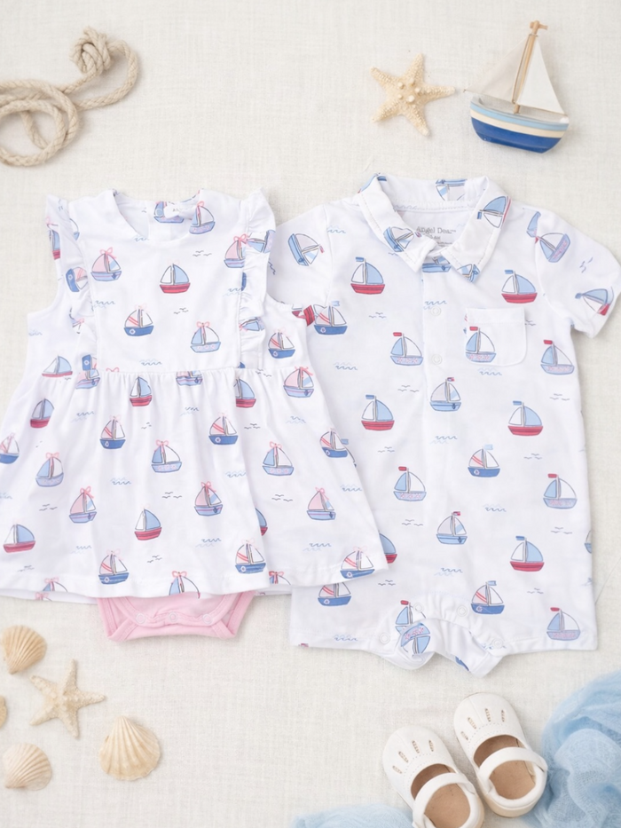 Two children's outfits with sailboat patterns, set against a light textured background with seashells and toys.