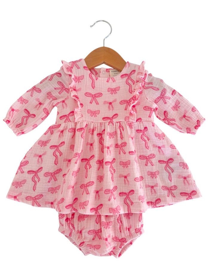 Pink dress with bow patterns, featuring ruffles and a matching diaper cover, displayed on a wooden hanger.