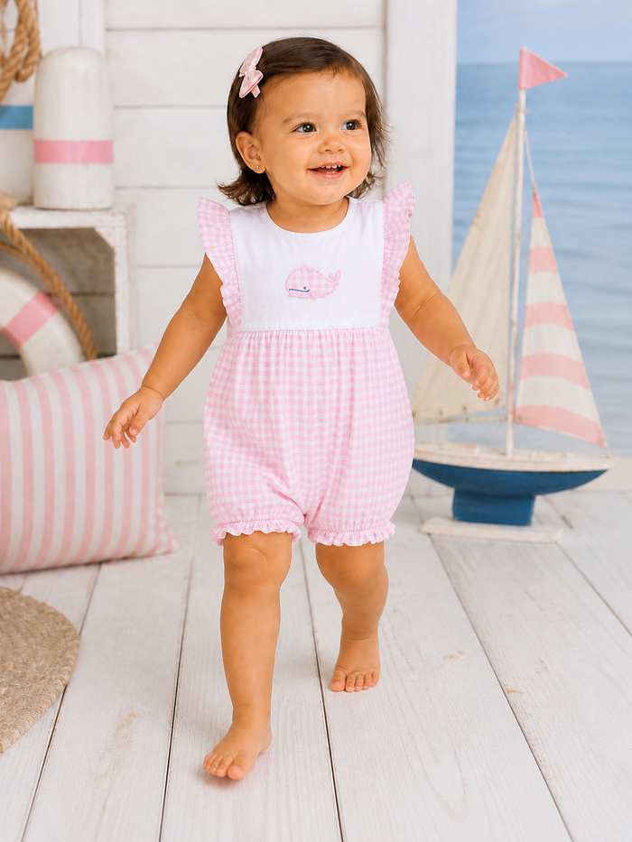 Smiling toddler in pink gingham outfit walking on a wooden floor with nautical decor in the background.