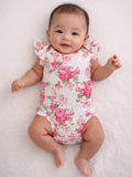 Smiling baby wearing a floral onesie, lying on a soft white blanket.