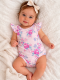Smiling baby girl in floral onesie and bow headband, sitting on a soft blanket.