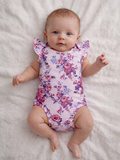 Smiling baby girl in floral onesie resting on a soft white blanket.