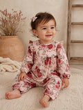Smiling toddler in floral pink romper, sitting on a textured rug with a natural background.