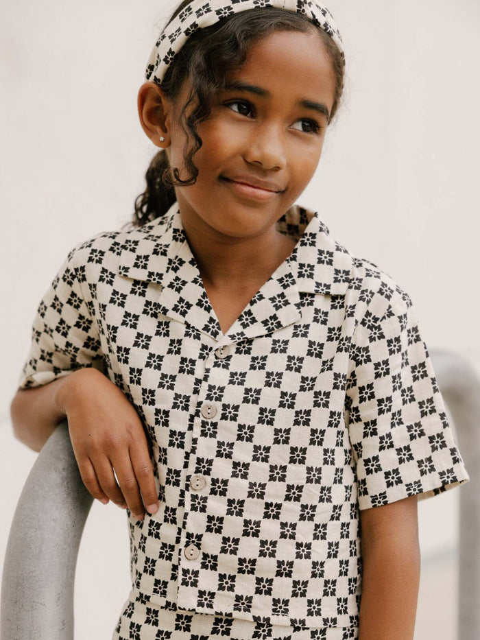 Young girl in patterned outfit, smiling and leaning on a railing, wearing a matching headband.