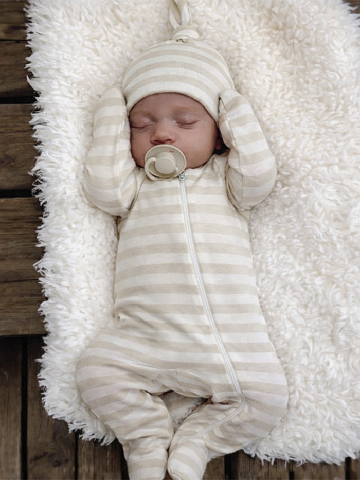 Sleeping baby in a striped outfit and hat, nestled on a fluffy white blanket.