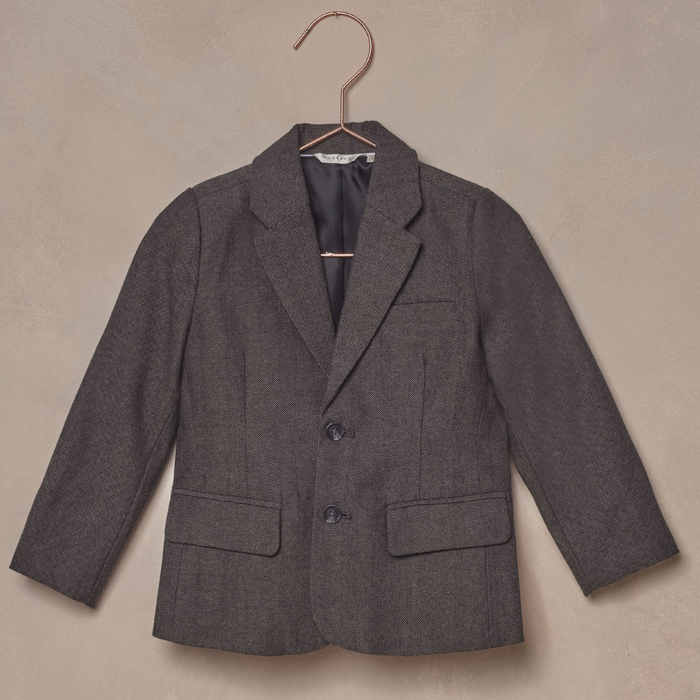 Gray children's blazer hanging on a rose gold hook against a textured background.