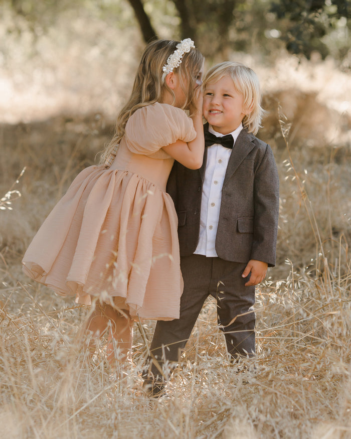 Two young children sharing a moment in a sunlit field, dressed elegantly for a special occasion.