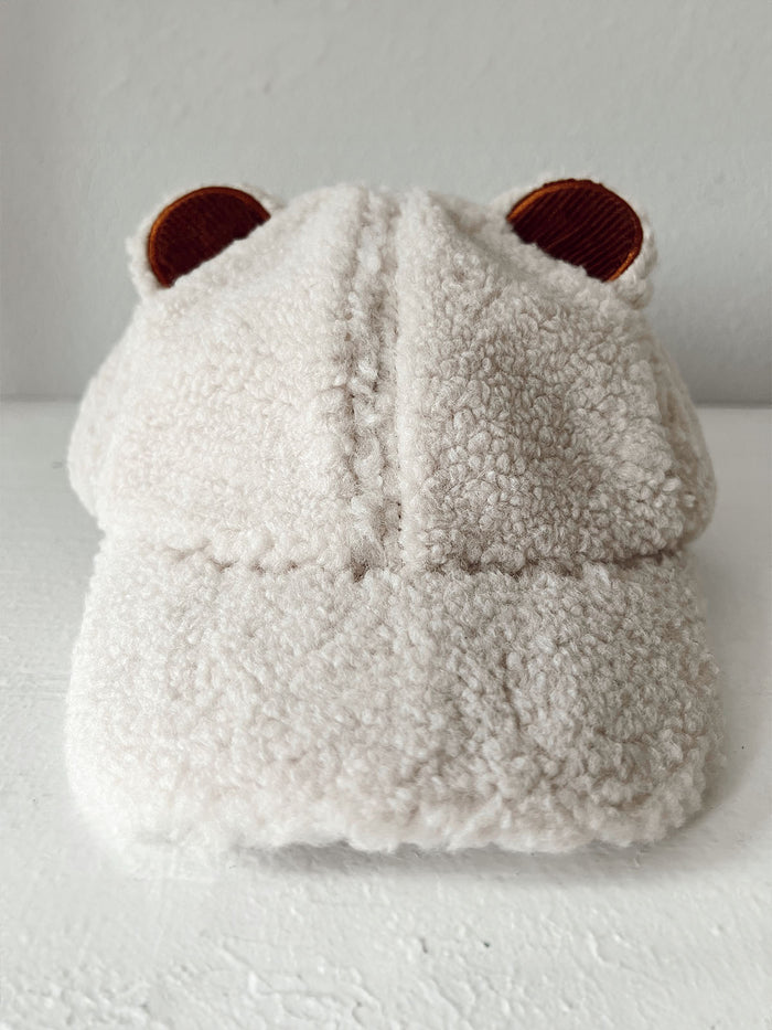 Fluffy beige cap with bear ears displayed on a white surface against a plain background.