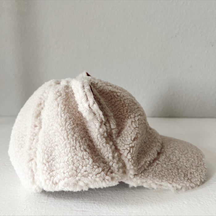 Side view of a soft beige furry cap resting on a white surface.
