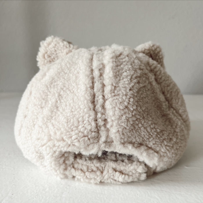 Beige fluffy hat with cat ears, displayed from the back on a light surface.