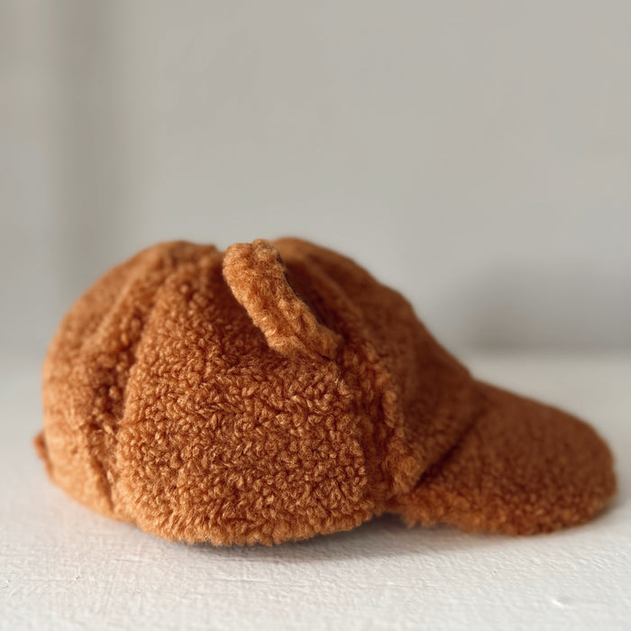 Soft, fluffy orange hat with a rounded top and curved brim, resting on a white surface.