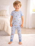 Smiling young boy in playful pajamas with cartoon patterns, standing in a bright, cozy bedroom.