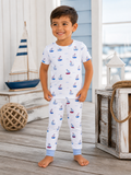 Smiling child in nautical-themed pajamas, standing by a sailboat and wooden decor in a coastal setting.