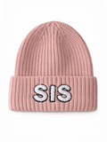 Pink knit beanie with "SIS" embroidered in white letters on the folded cuff.