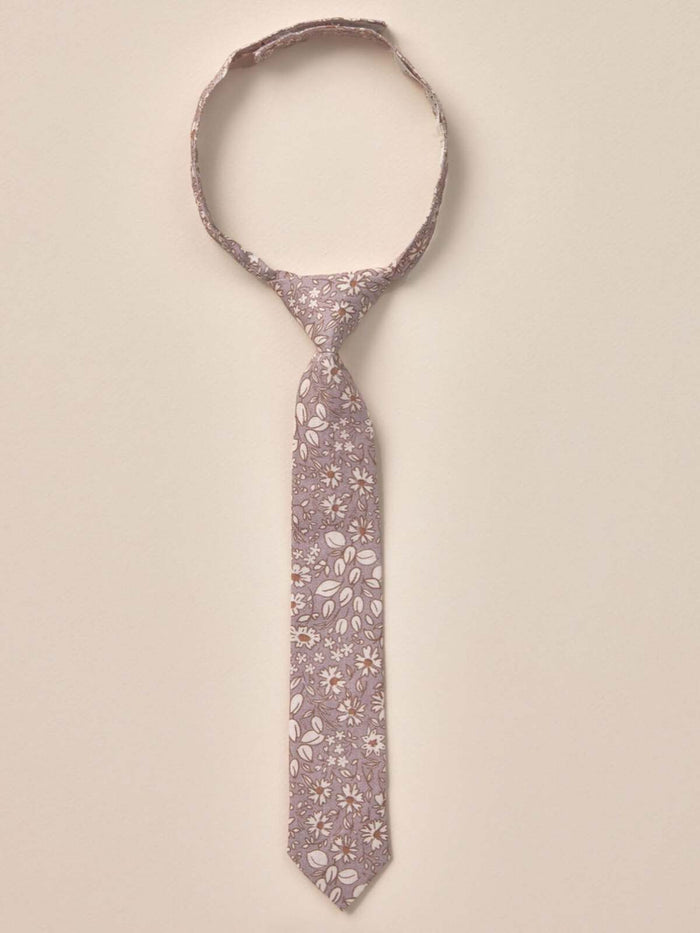 Floral patterned tie hanging against a neutral background, showcasing delicate leaves and blossoms.