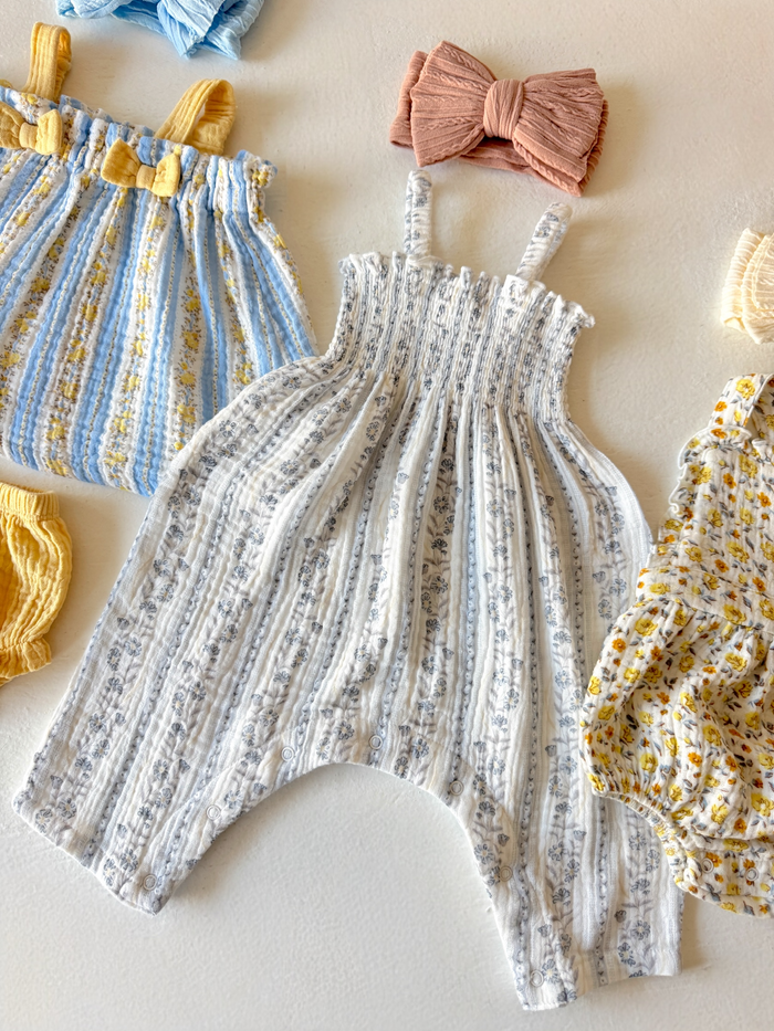 Child's fashion items including a light blue striped romper and floral print outfit, surrounded by headbands and accessories.