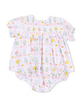 Floral baby romper with pink background and colorful flowers, featuring smocked yoke and ruffled sleeves.