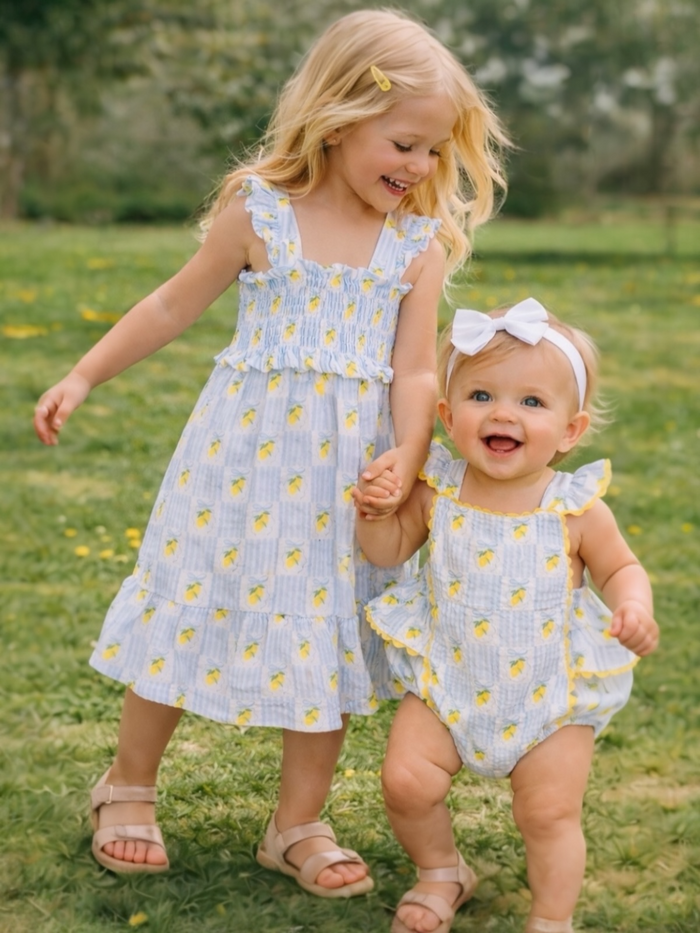 Two young children in playful floral outfits joyfully holding hands in a grassy field.