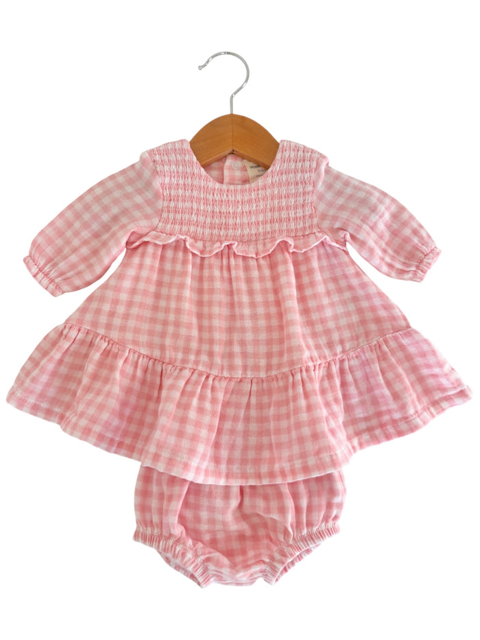 Pink gingham dress with long sleeves and ruffled hem, hung on a wooden hanger. Includes matching bloomer bottom.