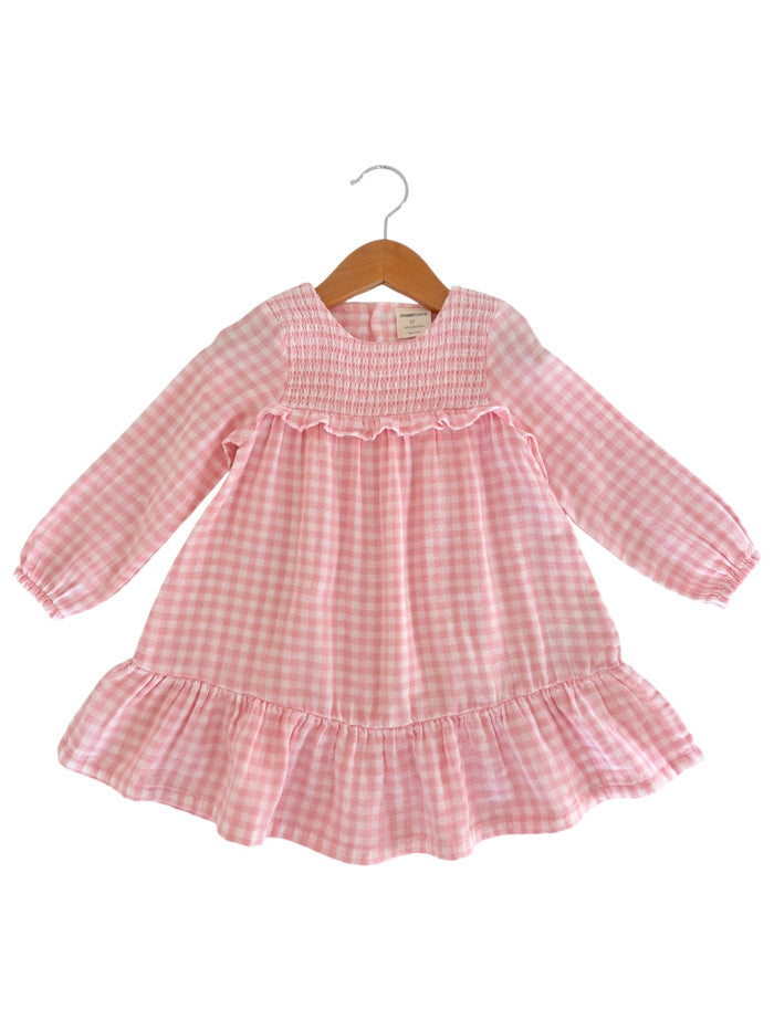 Pink gingham dress with long sleeves and ruffled hem, displayed on a wooden hanger.
