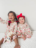 Two smiling young girls in matching holiday dresses, one holding a bunny toy, against a white background.