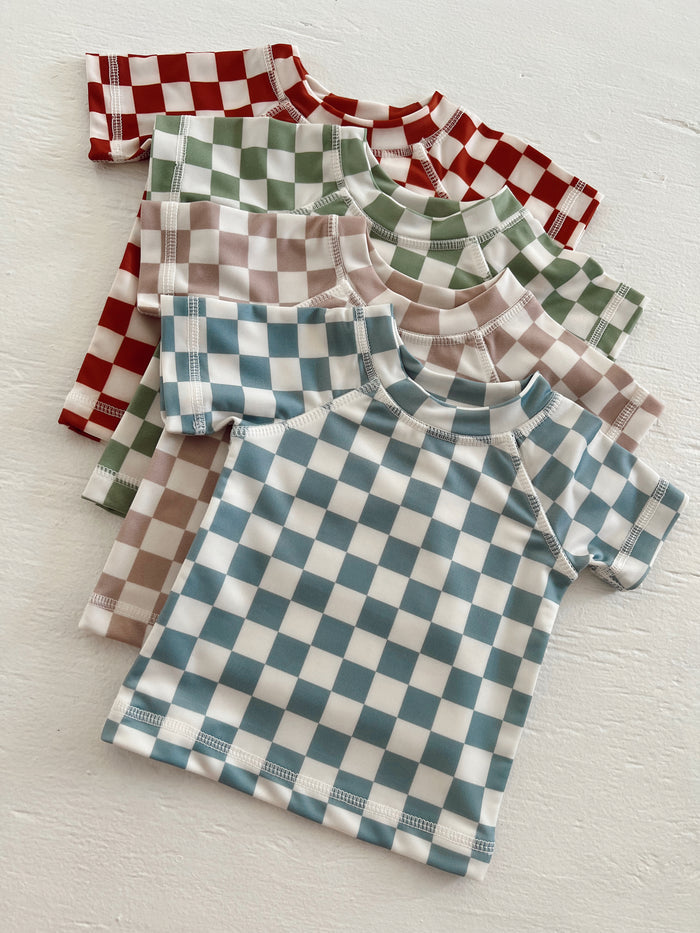 Four checkered t-shirts in red, green, brown, and blue stacked on a white surface.