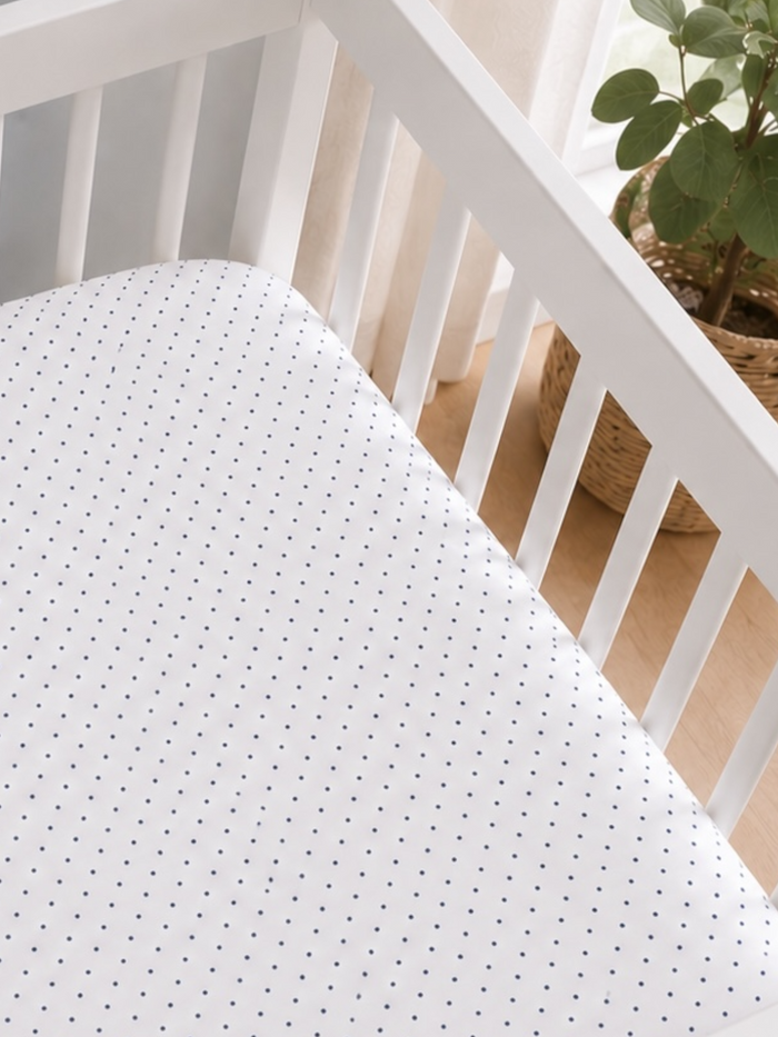 Crib with a white mattress featuring navy polka dots, illuminated by natural light from a nearby window.