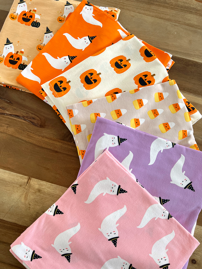Colorful Halloween-themed fabrics featuring ghosts, pumpkins, and candy corn patterns arranged on a wooden surface.