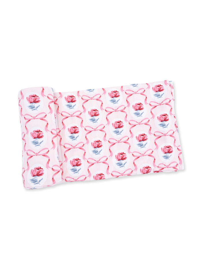 Rolled fabric featuring a pink floral pattern with ribbons on a white background.