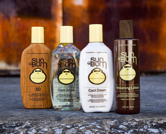 Four Sun Bum skincare products on a textured surface with a blurred natural background