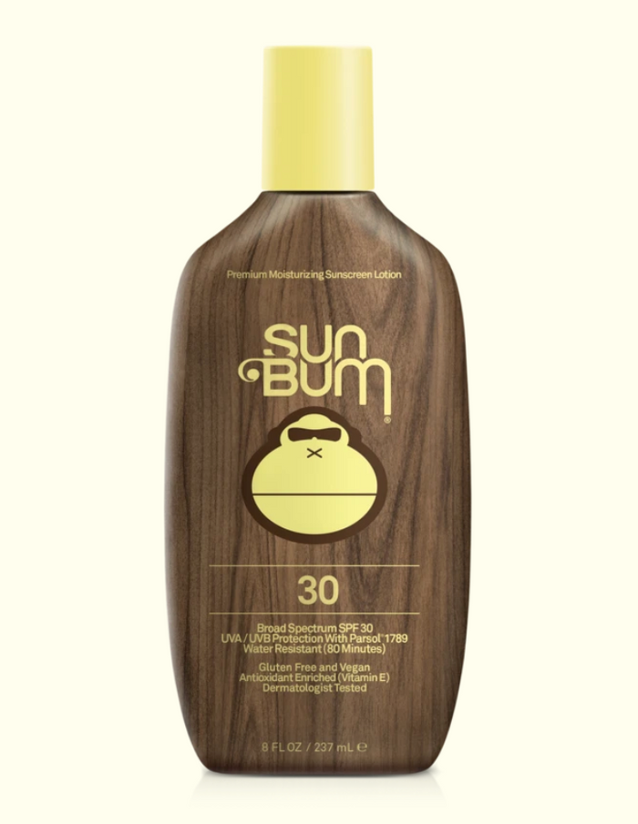 A series of four Sun Bum brand skin care products including sunscreen lotion, after sun cool down lotion, after sun cool down gel, and browning lotion, displayed outdoors.