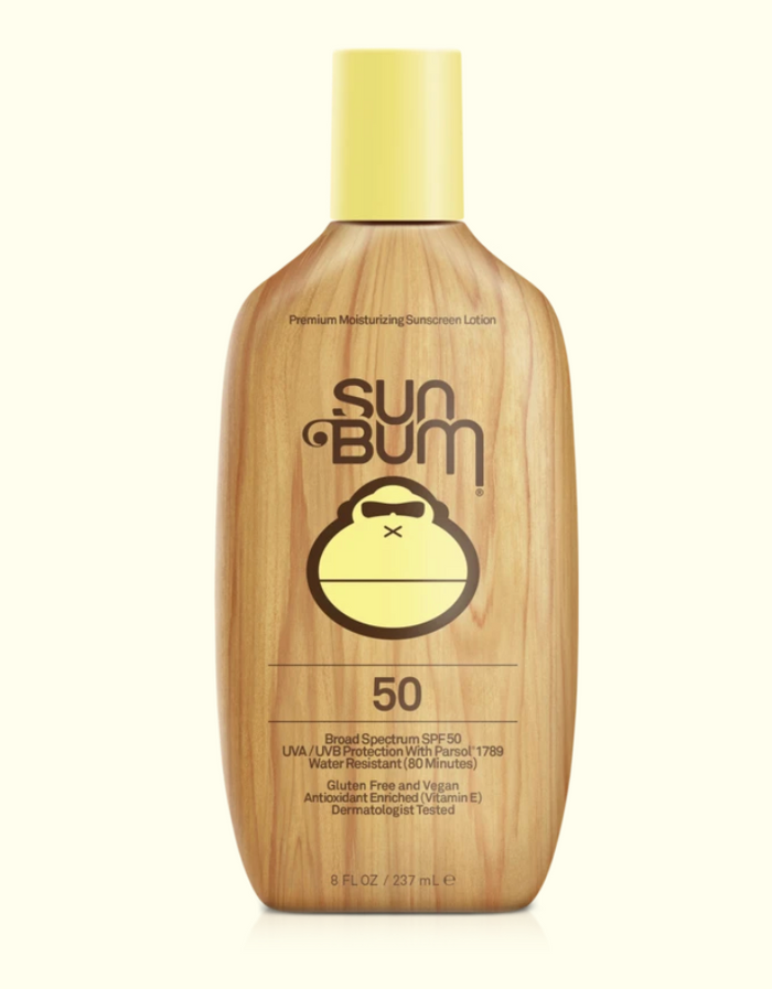 A series of four Sun Bum brand skin care products including sunscreen lotion, after sun cool down lotion, after sun cool down gel, and browning lotion, displayed outdoors.