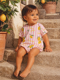 Smiling child in lemon-themed outfit sitting on stone steps with potted plants.