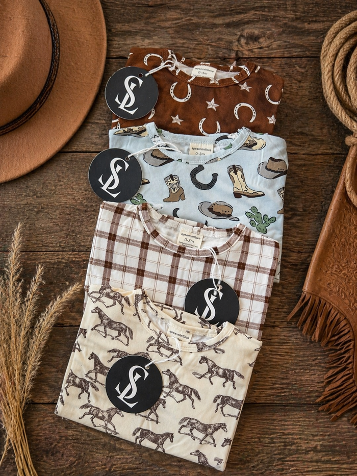 Four patterned shirts stacked on a wooden surface, with a hat and leather goods nearby.