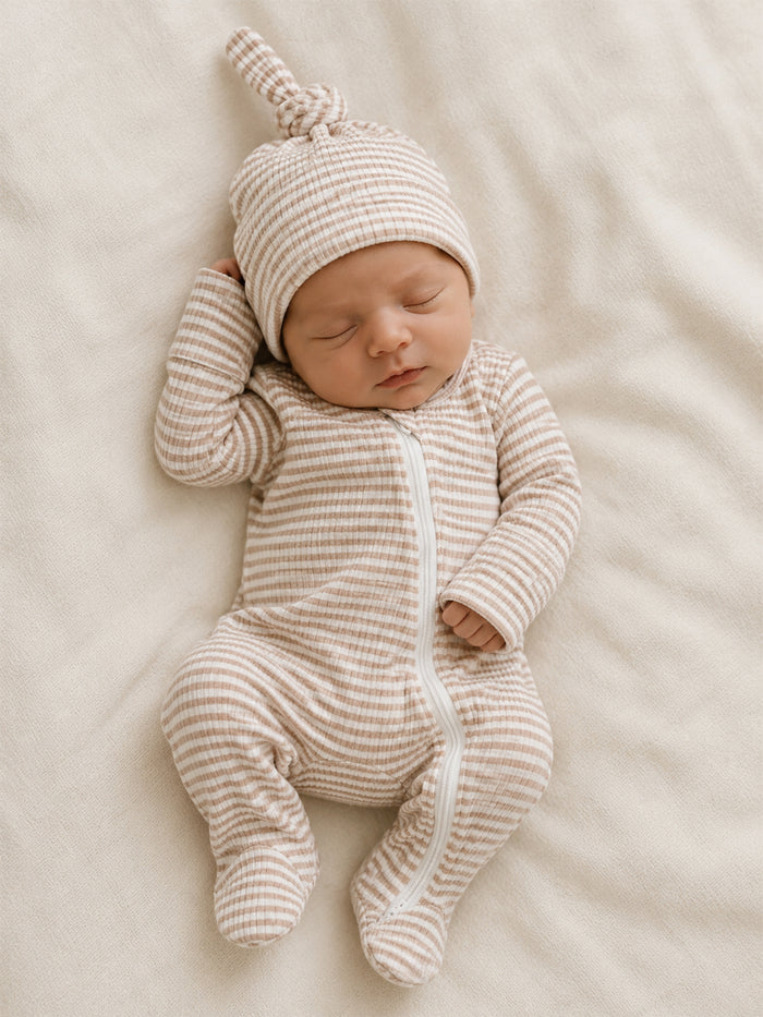 Newborn baby in a striped onesie and matching hat, peacefully sleeping on a soft, light-colored blanket.
