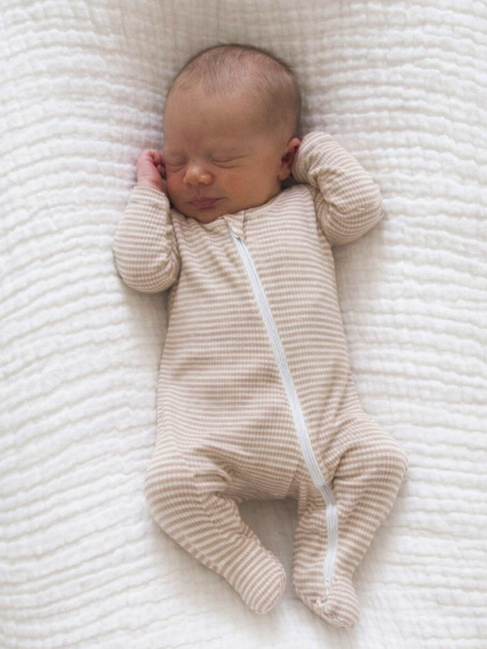 Newborn baby sleeping peacefully on a soft, textured blanket, wearing a striped zip-up onesie.
