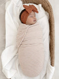 Newborn wrapped in a striped blanket, peacefully sleeping in a cozy basket with a soft knit blanket.