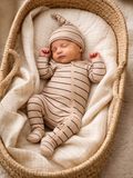 Sleeping newborn in a beige striped outfit resting peacefully in a woven basket on soft fabric.