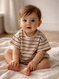 Smiling baby sitting on a soft blanket, wearing a striped t-shirt, with a neutral background.