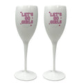 Two individuals holding clear plastic champagne glasses, wearing pink outfits, with one holding a phone and both smiling.