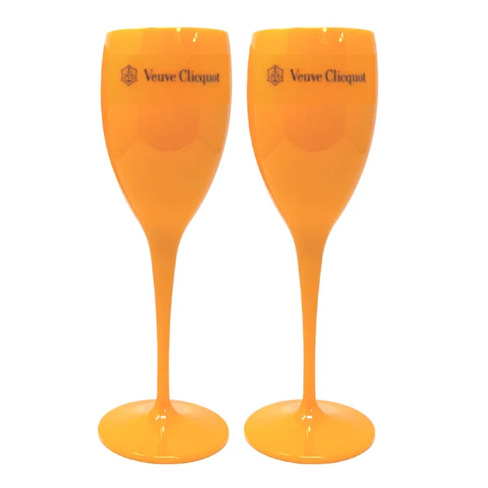 Two individuals holding clear plastic champagne glasses, wearing pink outfits, with one holding a phone and both smiling.