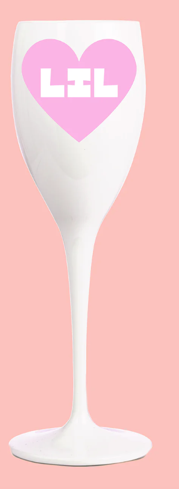 Two individuals holding clear plastic champagne glasses, wearing pink outfits, with one holding a phone and both smiling.
