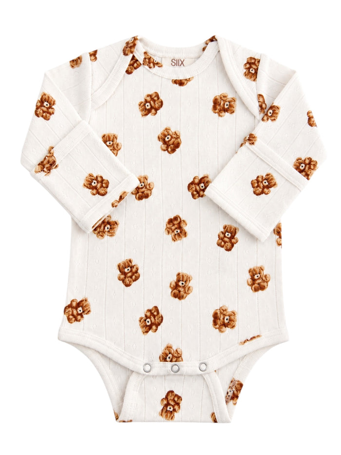 White baby onesie with teddy bear pattern on a textured background. Ideal for infants, cozy and stylish.