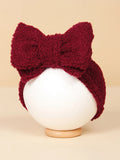 Burgundy fuzzy headband with a large bow, displayed on a white spherical mannequin against a soft beige background.