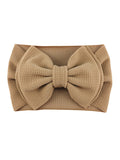 Tan headband with a large bow design, made from textured fabric. Perfect for adding a stylish touch.