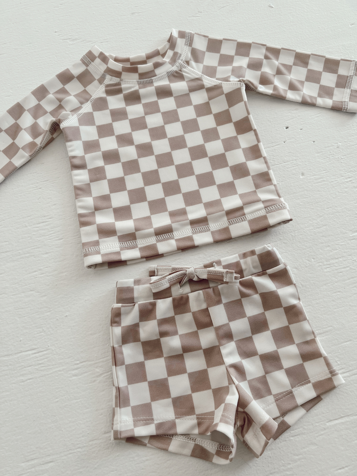 Brown and white checkered toddler swim shirt and shorts set on a light surface.