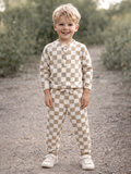 Smiling child wearing brown and cream checkered pajamas, standing outdoors on a gravel path.