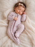 Sleeping baby in striped onesie with a bow headband, resting on soft, textured fabric.