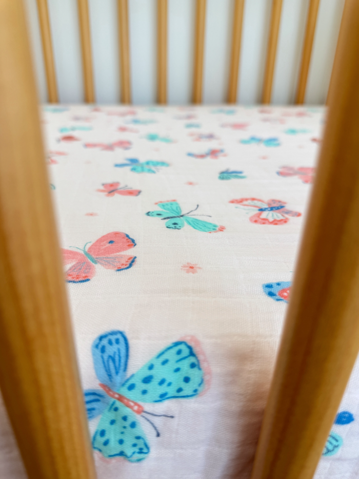 Colorful butterfly pattern on a crib sheet seen through wooden crib bars.